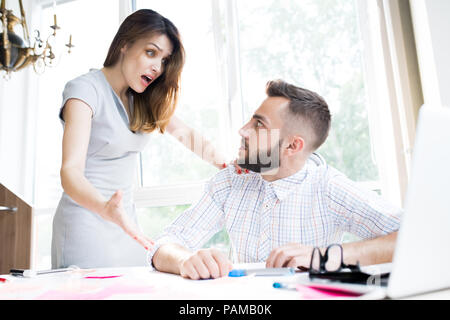 Portrait von aufgeregten Geschäftsfrau schockiert schauen, während sie etwas erklären, gutaussehenden Kollegen am Schreibtisch im Büro sitzen Stockfoto