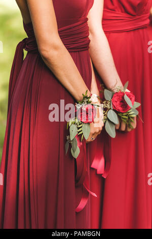 Blume Armbänder mit roten Rosen und seidenbändern. Brautjungfern in roten Kleidern, amerikanische Hochzeit Stockfoto