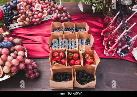 Satz von verschiedenen frischen Beeren in kleinen Handwerksbetrieben Papier Boxen auf Hochzeitsfeier Tabelle, rustikaler Stil, Sommer Stimmung Stockfoto