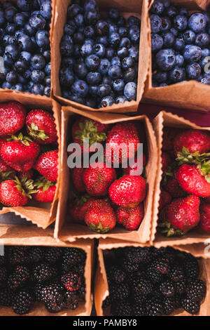 Satz von verschiedenen frischen Beeren in kleinen Handwerksbetrieben Papier Boxen auf Hochzeitsfeier Tabelle, rustikaler Stil, Sommer Stimmung Stockfoto