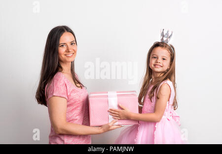 Ein kleines Mädchen mit Krone Kopfbügel und ihre Mutter mit einem Geschenk in einem Studio. Stockfoto