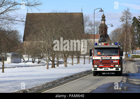 Scania 93 M fire truck fährt auf der Straße in der Dorfmitte Vergangenheit Pernio mittelalterliche Kirche im Hintergrund. Pernio, Salo, Finnland - 18. März 2018. Stockfoto