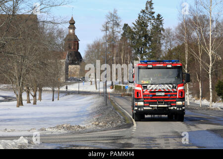 Scania Feuerwehrauto Laufwerke in Pernio Dorfzentrum beim Tag der offenen Tür Veranstaltung, die mittelalterliche Kirche auf dem Hintergrund. Pernio, Salo, Finnland - 18. März 2018. Stockfoto