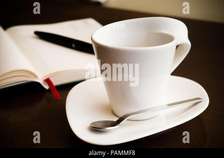 Kaffee am Arbeitsplatz mit einem leeren Journal auf dem Hintergrund Stockfoto