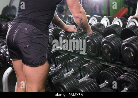 Die Hand des starken Mannes nimmt eine schwere Hantel in der Turnhalle. Stockfoto