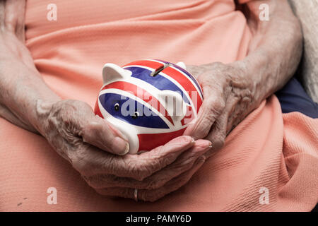 UK Pension, alte Frau Hände halten Sparschwein mit britischer Flagge Stockfoto