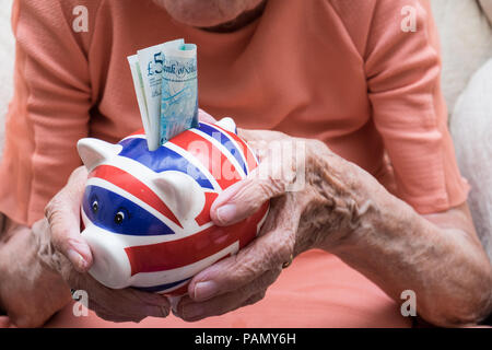 Altersvorsorge, fünf Pfund Hinweis im sparschwein von älteren Händen gehalten Stockfoto