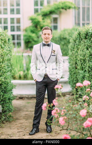 In voller Länge Foto des Bräutigams halten sie die Hände in den Taschen im Garten. Stockfoto