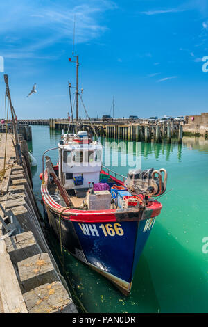 Ein kleines Fischerboot Mauren am Kai seinen Fang in der aqua grün Gewässern der West Bay in Dorset zu entladen. Stockfoto