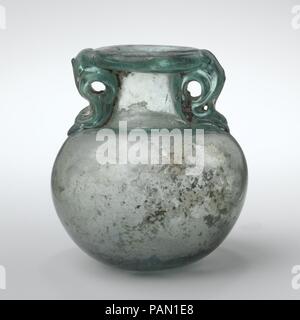 Glas aryballos (Öl Flasche). Kultur: Roman. Abmessungen: H.: 2. (5,1 cm). Datum: 2.-3.Jh. N.CHR.. Transluzent blau grün; Griffe in der gleichen Farbe. Dick, teilweise tubular Rim, gefaltet, unten, rund, und in auf der Oberseite abgeflacht; zylindrische Hals; horizontale Schulter; kugelförmigen Körper; Dick unten mit zentralen Kick und pontil Mark; zwei Dolphin Griffe angewendet zu übernehmen, bis der Hals an der Unterseite des Rim gezeichnet, stellte sich heraus, rund, und Unten, die Bohrungen zum Ring, und dann eine zweite Spur bis zum Ende der Felge beantragt, über Griffe gezeichnet, und verlor sich nach oben. Intakt; ein paar kleine b Stockfoto