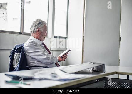 Ältere Unternehmer arbeiten im Büro. Über Internet auf dem Smartphone. Stockfoto