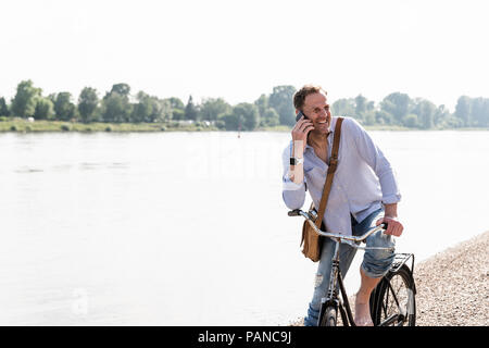 Reifer Mann mit Fahrrad mit an Rhein Ufer smartphone Stockfoto