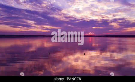 Antenne drone Panoramablick auf bunten lila Sonnenuntergang am See, Sonne Reflexion im Wasser, bewölkter Himmel nach Regen ohne Wind, zwei Männer in sp Stockfoto