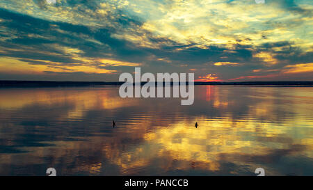 Antenne drone Panoramablick auf bunten natürlichen Sonnenuntergang am See, Sonne Reflexion im Wasser, bewölkter Himmel nach Regen ohne Wind, zwei Männer in s Stockfoto