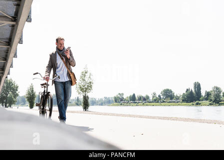 Reifer Mann mit Fahrrad mit an Rhein Ufer smartphone Stockfoto