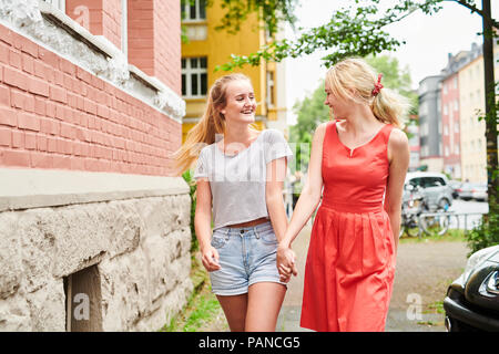 Zwei glückliche junge Frauen gingen Hand in Hand in der Stadt Stockfoto
