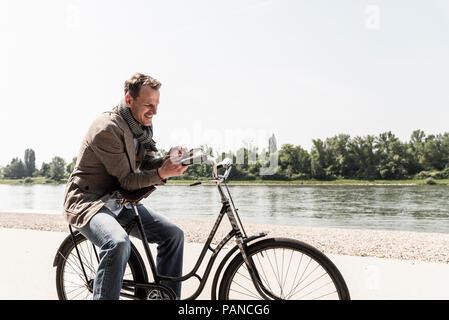 Reifer Mann mit Fahrrad mit an Rhein Ufer smartphone Stockfoto