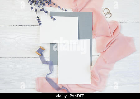 Weiße leere Karte mit zwei Trauringe auf einem Hintergrund von rosa Stoff mit Lavendelblüten und kalligraphischen Stift auf einem weißen Hintergrund. Mockup mit Umschlag und eine leere Karte. Flach. Ansicht von oben Stockfoto