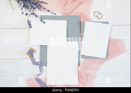 Weiße leere Karte mit zwei Trauringe auf einem Hintergrund von rosa Stoff mit Lavendelblüten und kalligraphischen Stift auf einem weißen Hintergrund. Mockup mit Umschlag und eine leere Karte. Flach. Ansicht von oben Stockfoto
