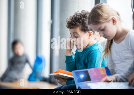 Müde Schüler mit Buch in der Schule Stockfoto