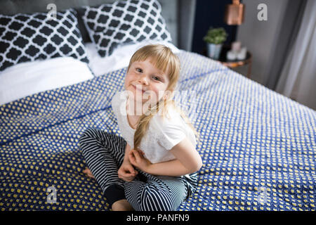 Blonde Mädchen sitzt auf dem Bett und lächelte, Stockfoto