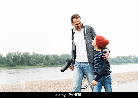 Gerne Vater und Sohn gehen mit Einrad am Flußufer Stockfoto