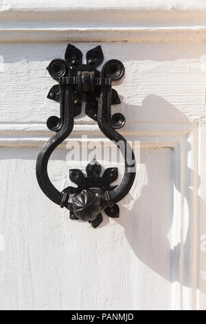 Reich verzierte schwarze Metall Türklopfer auf weiß lackierten Holz- abgeschrägten Tür montiert auf Eigentum in Perast, Montenegro an einem sonnigen Tag und an den Schatten. Stockfoto