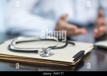 Dateien und Stethoskop auf dem Schreibtisch in der medizinischen Praxis mit Arzt im Hintergrund Stockfoto