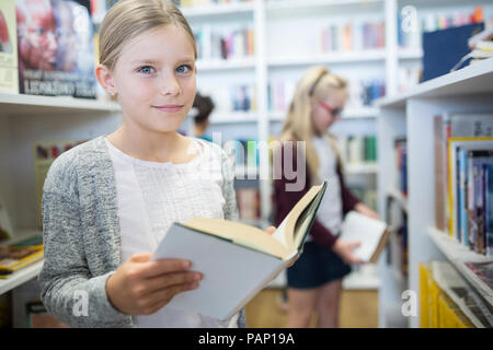 Portrait von lächelnden Schulmädchen mit Buch in der Bibliothek Stockfoto