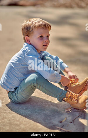 Junge sitzt im Freien Schnürung seine Stiefel Stockfoto