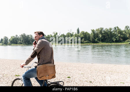 Reifer Mann mit Fahrrad mit an Rhein Ufer smartphone Stockfoto