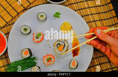 Der Mensch isst Sushi mit Stäbchen. Nahaufnahme der Hand essen Traditionelles japanisches Essen mit Stäbchen. Stockfoto