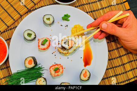 Essen roll Sushi japanisches Restaurant, Hand mit Stäbchen close-up. Die Hand eines Mannes holding Sushi mit Stäbchen. Stockfoto