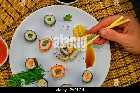 Der Mensch isst Sushi mit Stäbchen. Nahaufnahme der Hand essen Traditionelles japanisches Essen mit Stäbchen. Stockfoto