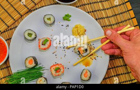 Essen roll Sushi japanisches Restaurant, Hand mit Stäbchen close-up. Die Hand eines Mannes holding Sushi mit Stäbchen. Stockfoto