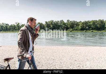 Reifer Mann mit Fahrrad mit an Rhein Ufer smartphone Stockfoto