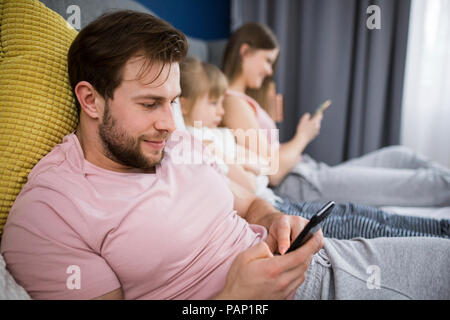 Vernachlässigte Mädchen sitzen auf dem Bett mit ihren Eltern, mit Smartphones Stockfoto