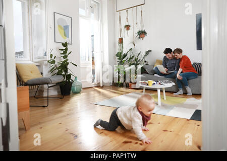 Die Eltern sitzen auf der Couch, mit Laptop, während Tochter spielen auf dem Boden ist Stockfoto