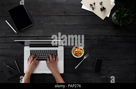 Person mit Laptop und Snack am Schreibtisch sitzen Stockfoto