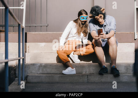 Paar in der Verkleidung sitzt auf der Treppe, mit Smartphone Stockfoto