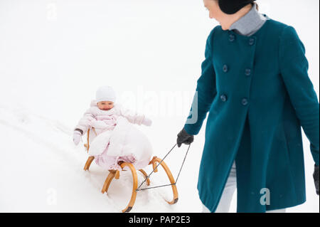 Mutter ziehen kleine Tochter auf Schlitten Stockfoto