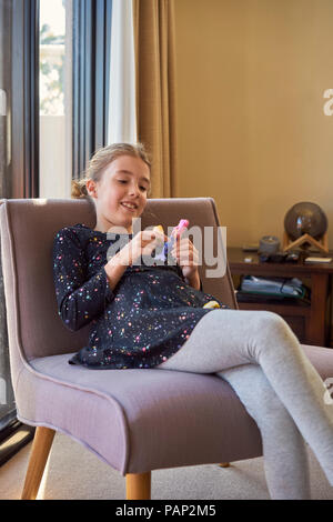 Lächelnde Mädchen sitzt auf einem Sessel zu Hause spielt mit Puppe Stockfoto