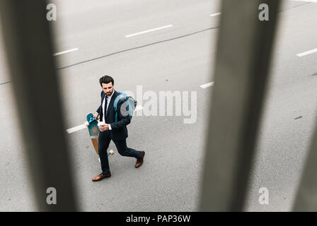 Geschäftsmann mit Takeaway Kaffee und Skateboard zu Fuß auf der Straße Stockfoto