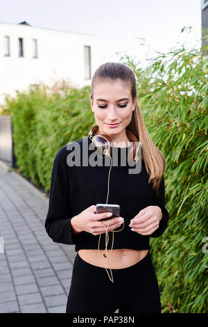 Sportliche junge Frau mit Kopfhörer und Handy im Freien Stockfoto