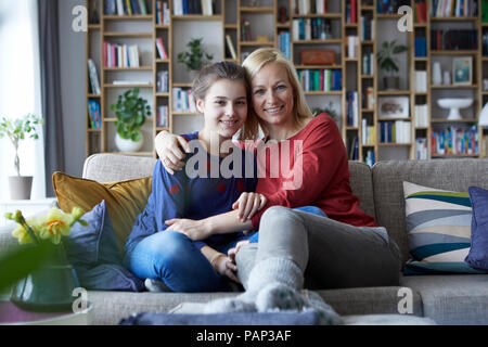 Mutter und Tochter sitzen am Tisch mit Arme um Stockfoto