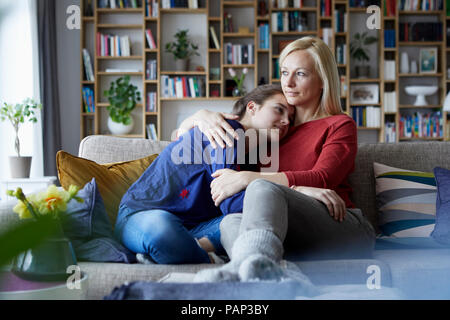 Mutter und Tochter sitzen am Tisch mit Arme um Stockfoto