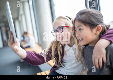 Gerne Schülerinnen nehmen einer selfie mit Tablette auf Schule Korridor Stockfoto