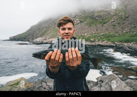 Norwegen, Lofoten, Moskenesoy, junger Mann mit frisch gefangenen Fisch bei Horseid Strand Stockfoto