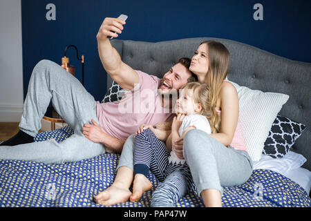 Glückliche Familie sitzt auf dem Bett, unter Smartphone selfies Stockfoto