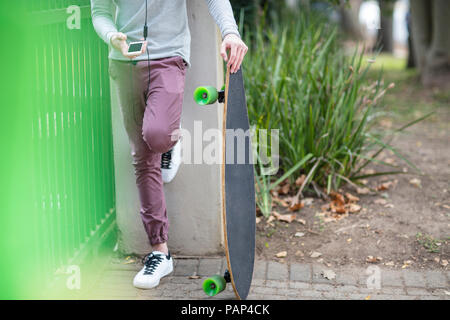 Close-up boy Holding Skateboard und mit Handy Stockfoto